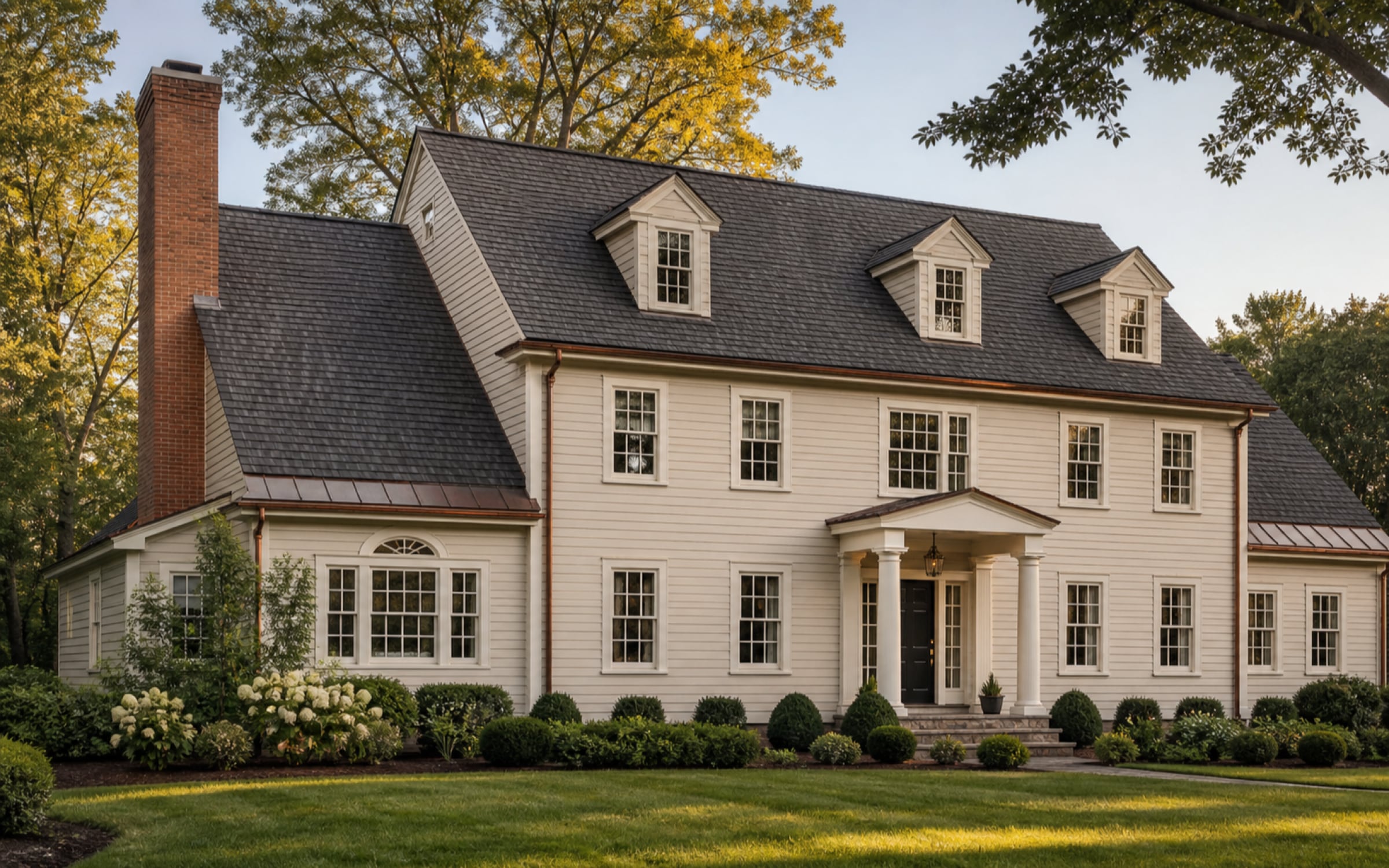 A two-storey colonial with a new charcoal architectural shingle roof, three dormers and copper downspouts, photographed from the front lawn